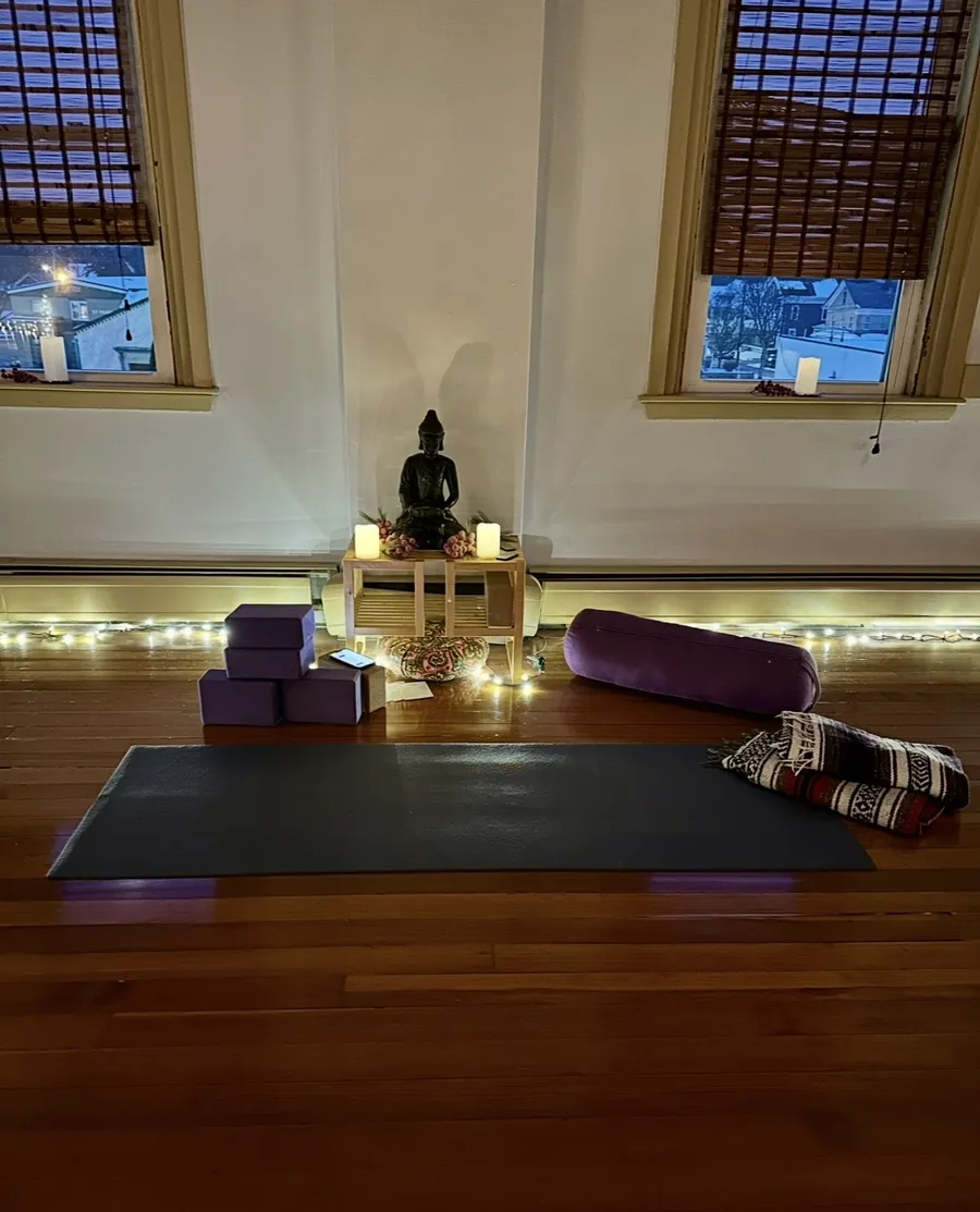 Candlelit Buddha altar with bolster, blocks, blanket and a mat set out on the studio floor