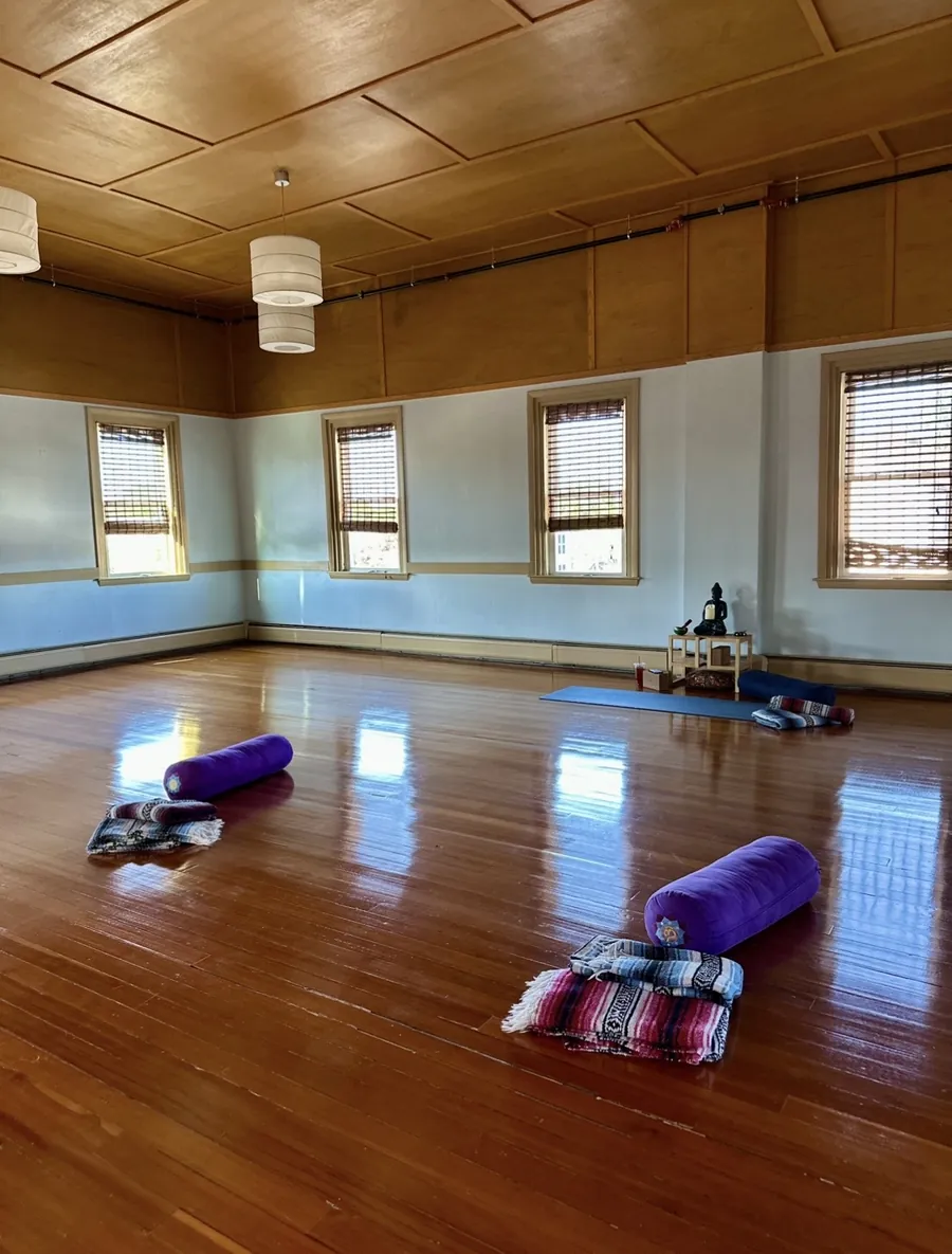 Empty practice room with wood floors, bolsters and blankets ready for a restorative class